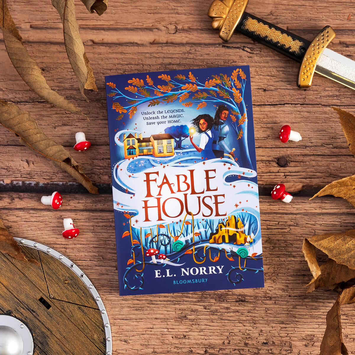 Fablehouse book surround by decorative woodland items, including toadstools, and a sword.