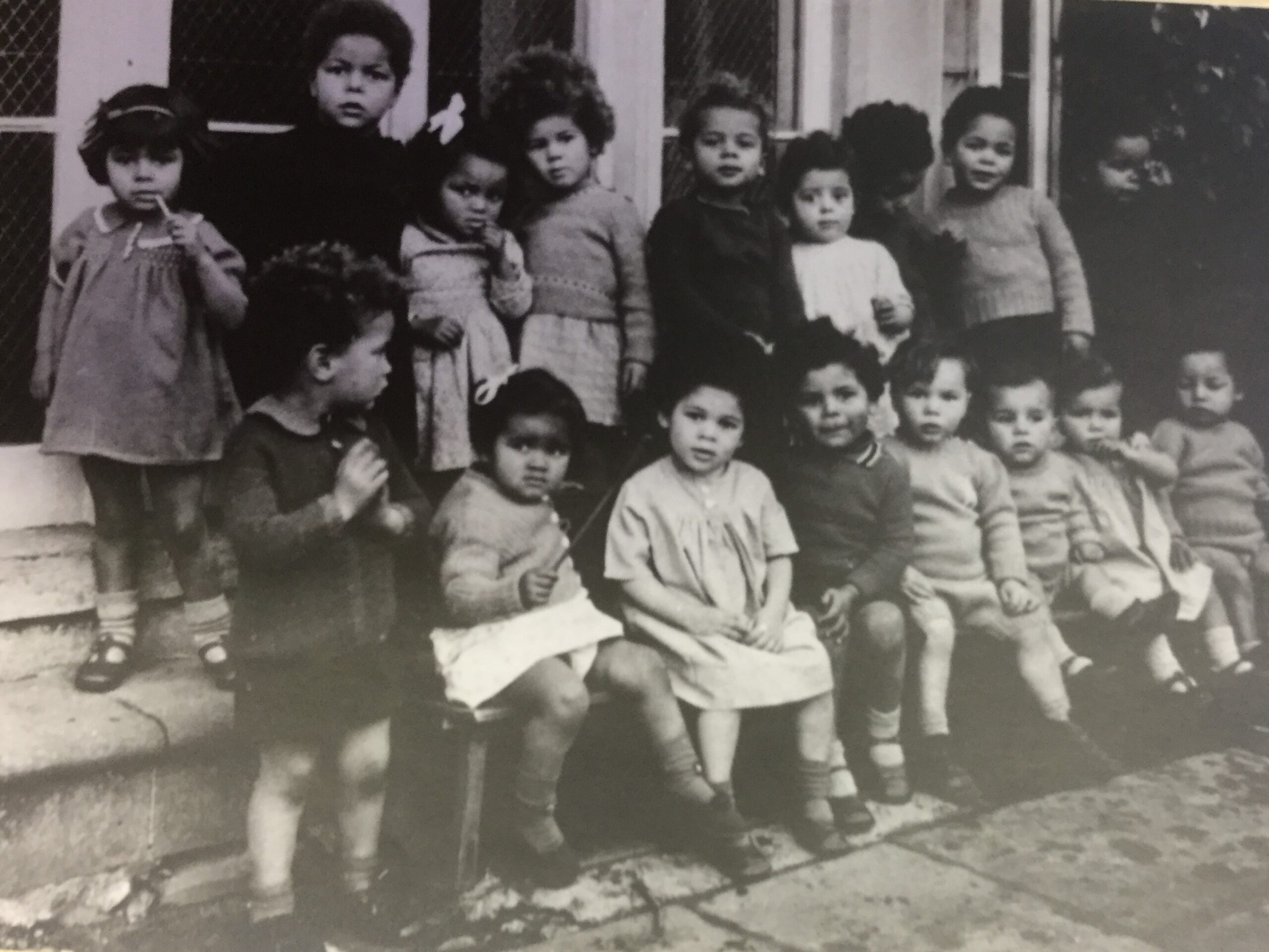Black and white photograph of around 20 mixed race children standing outsdie a building in the 1940s.
